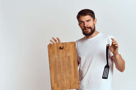 Man with a kitchen wooden board and with a shovel on a light background emotions white t-shirt modelの写真素材