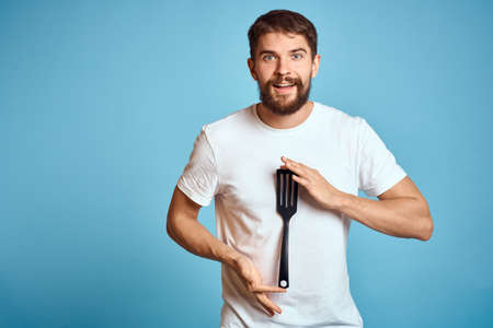 A man with a shovel for cooking in his hand on a blue background and a white T-shirtの写真素材