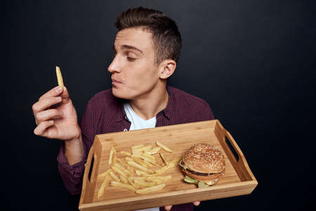 man holding wooden pallet with fast food in his hands diet food hunger lifestyle dark backgroundの写真素材