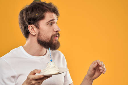 Handsome man with a beard and in a cap celebrating a birthday party yellow backgroundの写真素材