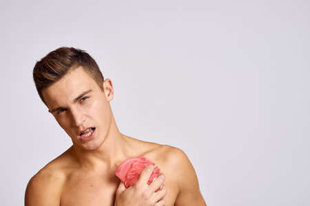 naked guy with a pink sponge in his hand washes his body on a light background cropped view
