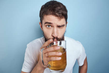 Cheerful man in a white T-shirt with a beer mug drunk blue background