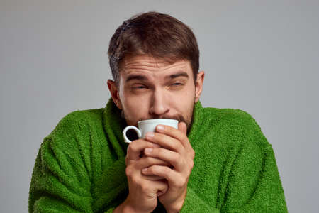 Man in a green robe with a cup of drink in his hands on a gray background cropped viewの写真素材