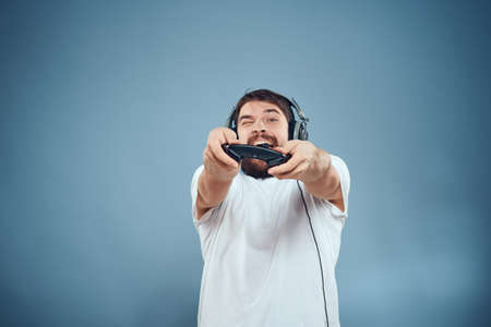 Man in headphones controller in hands playing game console lifestyle emotions blue background white t-shirtの写真素材