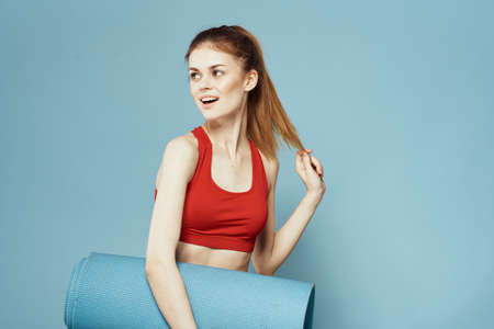 Sportive woman training mat in hands Red tank top exercise blue backgroundの写真素材