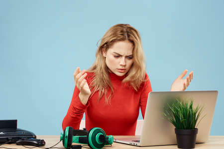 Woman sitting at a table in front of a laptop headphones controller playing online lifestyle blue backgroundの写真素材