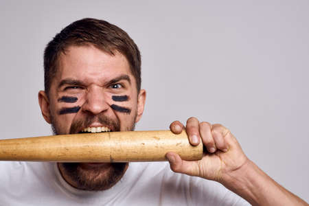 Aggressive man with a baseball bat in his hands on a gray background And makeup on his faceの写真素材
