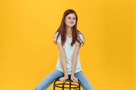 Woman sitting on a chair white t-shirt jeans fashionable clothes glamor studio yellow backgroundの写真素材