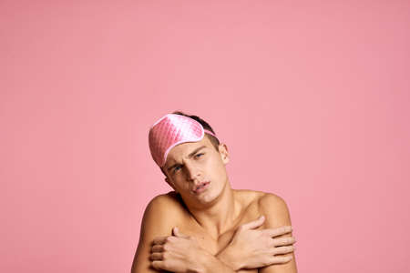 man in pink sleep mask on pink background naked shoulders morningの写真素材