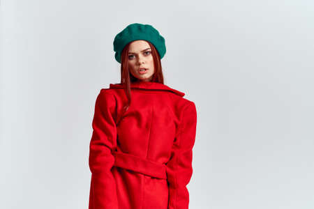 A woman holds in her hand a red coat and a dark T-shirt Green hat cropped view of a light backgroundの写真素材