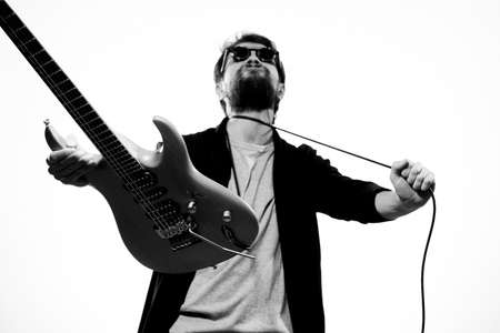 A man holds a guitar in his hands black leather jacket dark glasses music performance light backgroundの写真素材