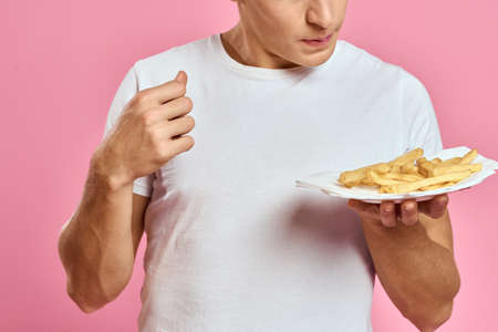 Man with French fries in a paper box on a pink background calories fast food portrait pink backgroundの写真素材