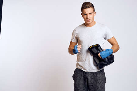 Strong man with boxing gloves and in a white t-shirt on an isolated background cropped view of the...