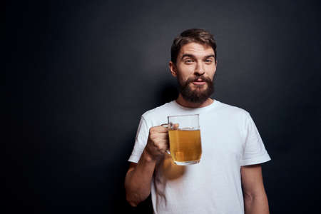 man with a mug of beer in a white t-shirt emotions lifestyle drunk on a dark isolated backgroundの写真素材