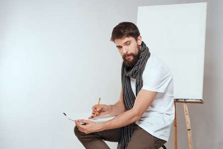 Male artist sitting on chair drawing brush easel hobby Creative light backgroundの写真素材