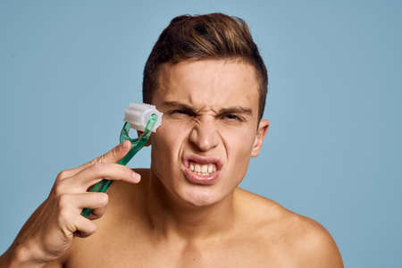 naked man with a massage instrument in his hand on a blue background emotions open mouth model