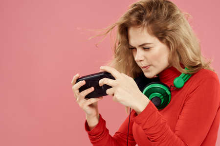 Woman with mobile set-top box headphones playing lifestyle pink background red jacket