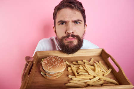Man with a tray of food in his hand hamburger fries and fast food calorie pink background portrait...