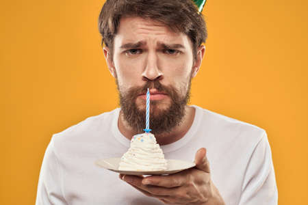 Handsome man with a beard and in a cap celebrating a birthday party yellow background