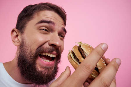 Portrait of a man with a hamburger on a pink background close-up cropped view of a modelの写真素材