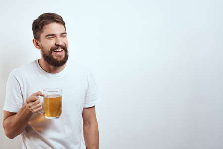man with a mug of beer in his hands and a white t-shirt light background mustache beard emotions modelの写真素材