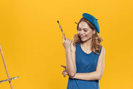 Artist woman in blue beret brush easel art drawing education hobby Creative approach yellow backgroundの写真素材
