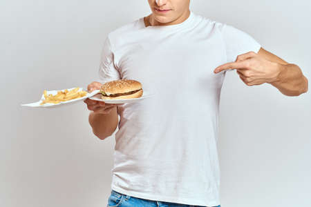 a man with fries and a hamburger on a light background in white t-shirt close-up cropped view Copy...