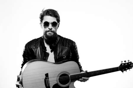A man plays the guitar in a black leather jacket with sunglasses on a light backgroundの写真素材