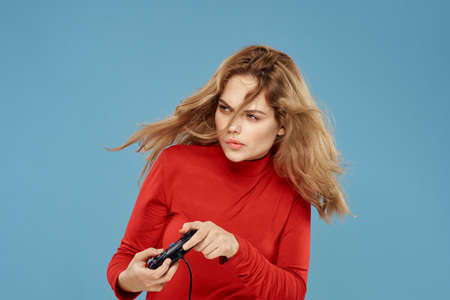 Pretty woman gamepad in hands playing games entertainment consoles to lifestyle blue background red jacketの写真素材