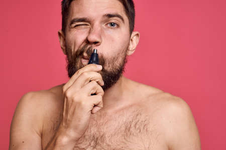 bearded man bare shoulders removes hair from nose body care pink backgroundの写真素材
