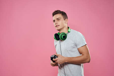 A man with a joystick in his hands headphones playing games entertainment lifestyle white t-shirt pink backgroundの写真素材