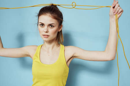Sportive woman holding a skipping rope yellow tank top exercise gymnastics blue background