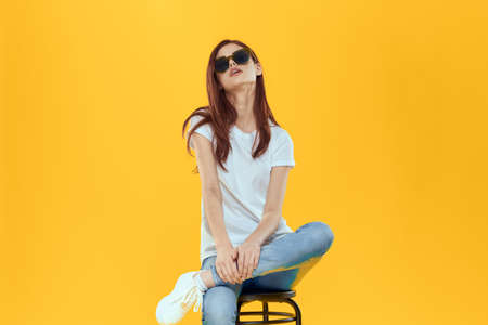 Pretty woman sits on a chair wearing sunglasses yellow background lifestyle