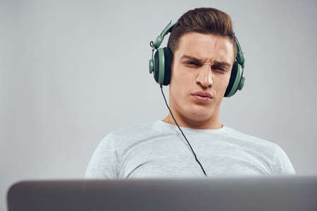 A man on the couch in front of a laptop with a joystick in a video game technology headphones
