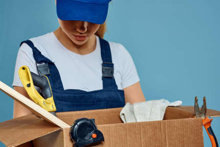 Working woman in uniform with box in hands tools loading delivery service blue background