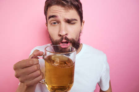 Drunk man with a large mug of beer On a pink background and a white T-shirt relaxed view of a thick...