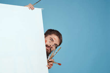 Male artist backs up behind easel brush art creativity blue background
