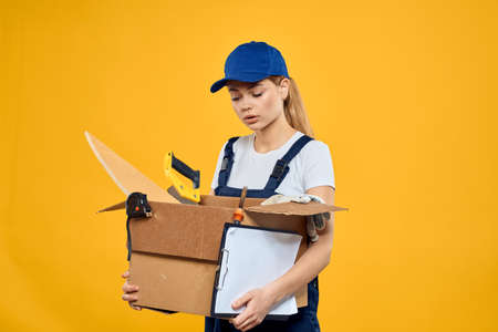 Woman with a box of construction tools and in a cap on a yellow background repair construction...
