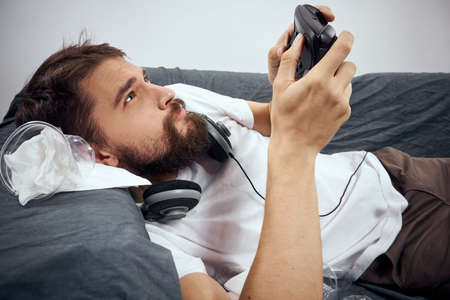 A man lies on the couch with gamepad headphones playing leisure lifestyle