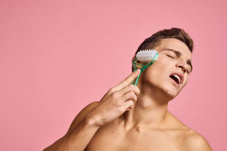 Handsome man with massager in hand on isolated pink background cropped view clean skinの写真素材