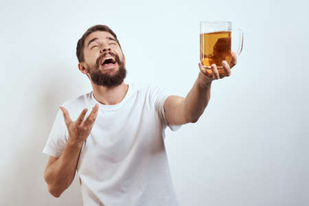 man with a mug of beer in his hands and a white t-shirt light background mustache beard emotions...
