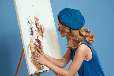 Woman artist paintbrush paint on canvas easel art education blue background