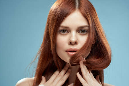 Pretty woman holding hair in hands grooming naked shoulders cropped view blue backgroundの写真素材