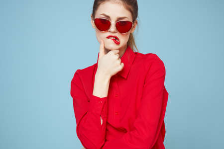 Beautiful woman in dark glasses red shirt bright makeup emotions attractive look blue background