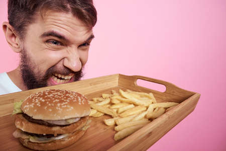Man with a tray of food in his hand hamburger fries and fast food calorie pink background portrait...