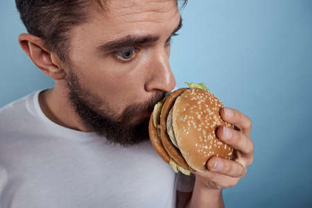 Emotional man hamburger fast food diet food close-up blue backgroundの写真素材