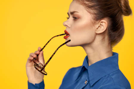 Portrait of a woman with glasses in her hands on a yellow background and in a blue shirt cropped viewの写真素材