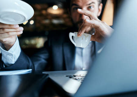 Business man sitting in a cafe with a cup of coffee in his hands in front of a laptop technology...