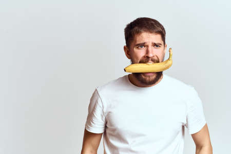 Cheerful man with a banana in his hands on a light background fun emotions Cropped view Copy Spaceの写真素材