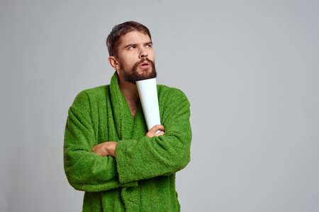 emotional man in a green dress with a rolled sheet of paper on a light background cropped viewの写真素材